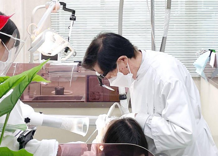 大野院長による虫歯治療中の写真‗歯科助手が口腔外バキュームをと、バキュームを持ちサポートしている写真